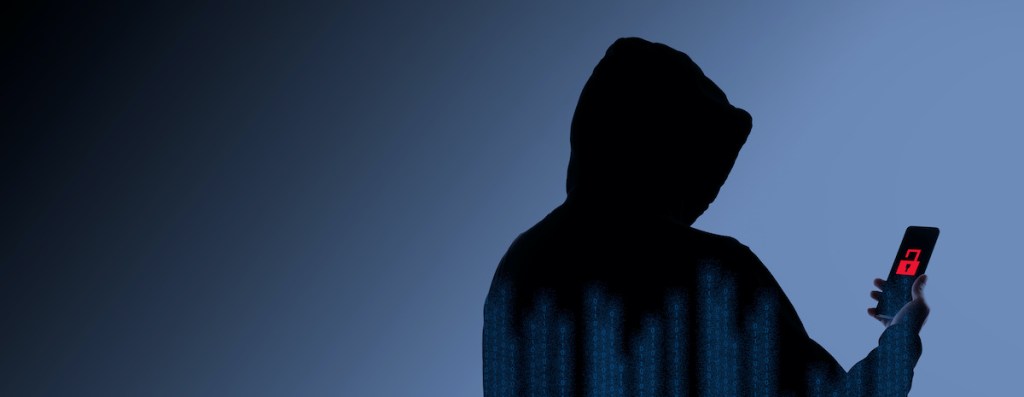 Hacker Anonymous and face mask with smartphone in hand. Man in black hood shirt holding and using mobile phone on white background. Represent cyber crime data hacking or stealing personal data concept